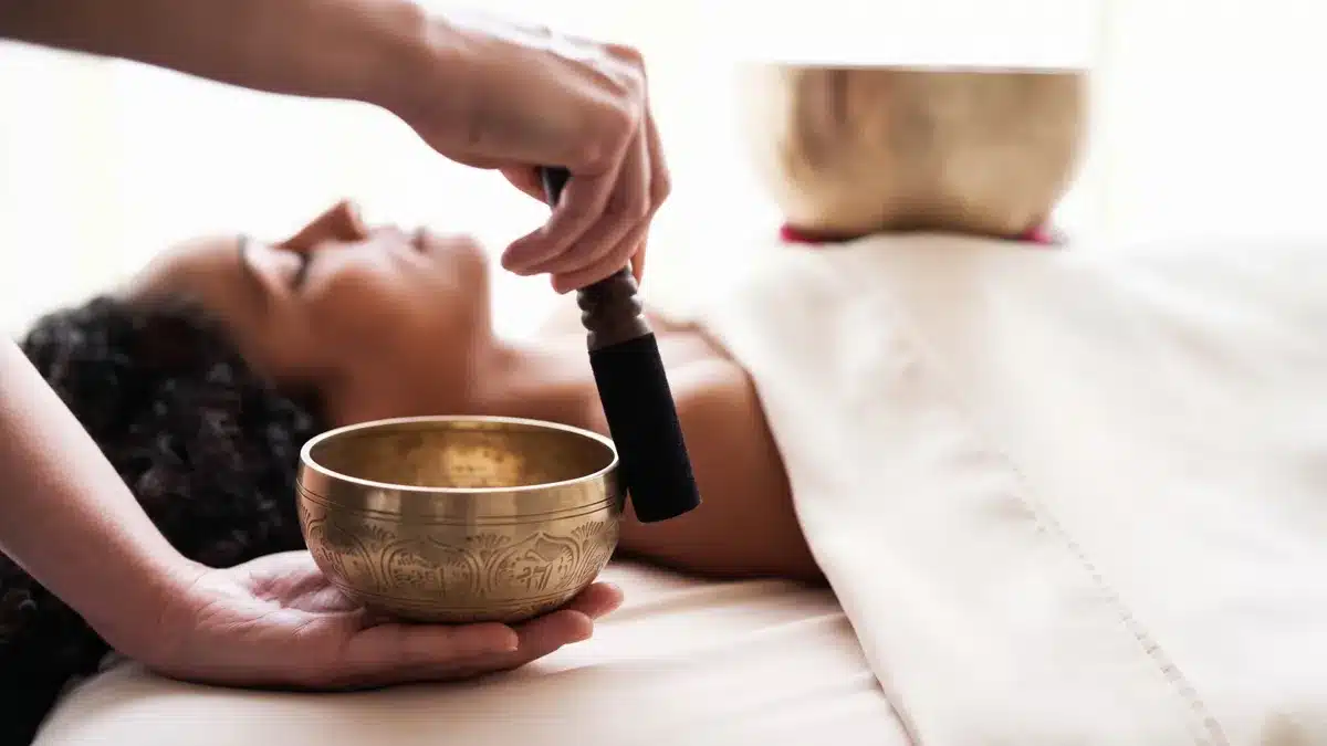 Sesión de baño de sonido con cuencos tibetanos: terapeuta tocando un cuenco junto a una mujer tumbada y relajada